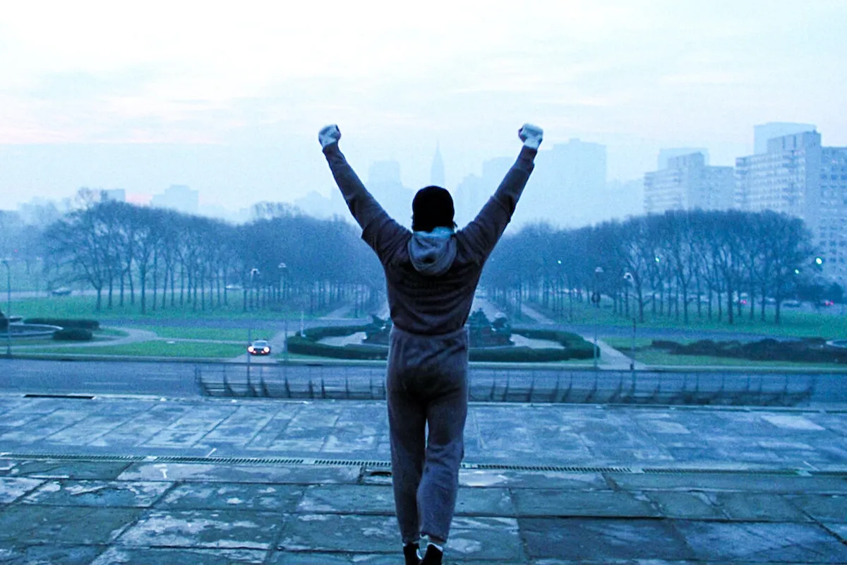 A solitary figure raises both arms triumphantly atop the Philadelphia Museum of Art steps at dawn — the iconic Rocky moment.